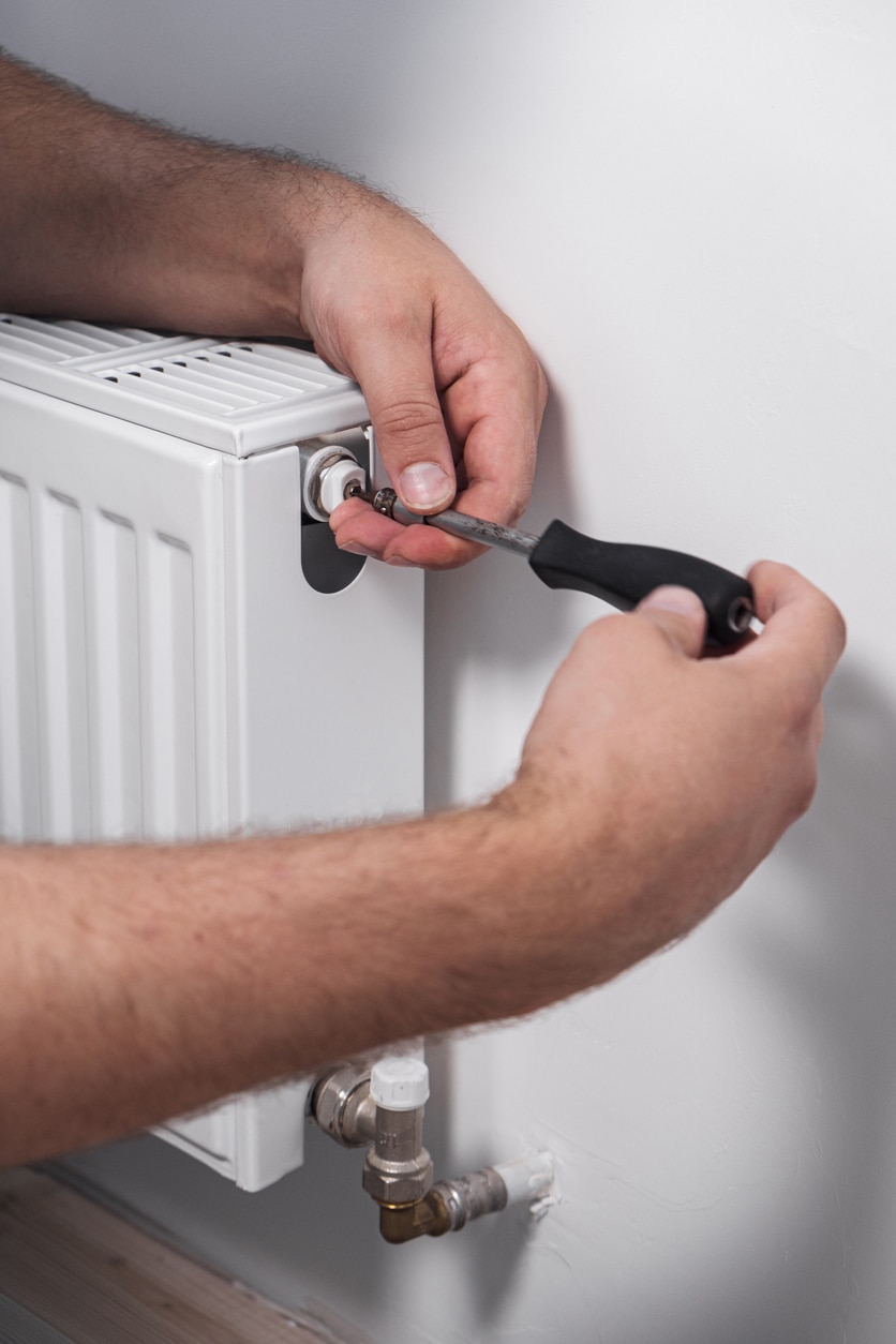 Plumber installing new steel hot water central heating radiator at home