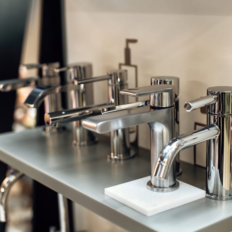 Group of modern stylish water taps for bathroom in showroom. Rows of new faucets in plumbing shop, closeup. Selective focus.