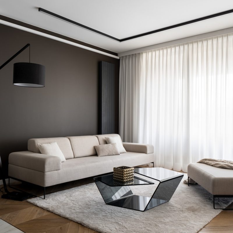 Classy and elegant living room with luxury, beige sofa, modern black coffee table and big window behind white curtains
